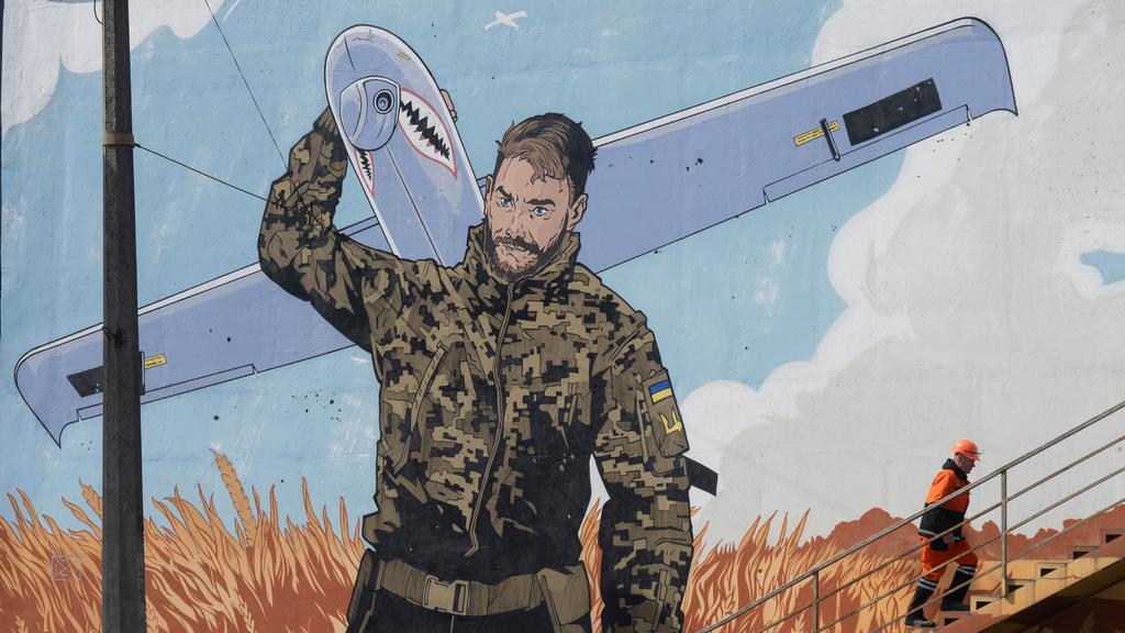 A municipal worker climbs stairs backdropped by a mural depicting a Ukrainian soldier carrying an Shark military drone.